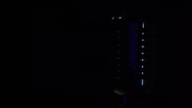 Spotlights shine on a chrome retro mic on black background and turn off. Professional classic vintage glare microphone for record or speak to audience on stage in dark empty club close up.