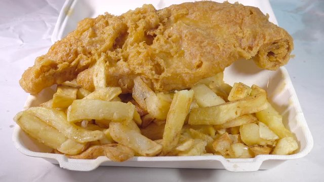 Slow motion close POV shot of drops of vinegar and salt, dropping onto a takeaway meal of deep fried battered fish and chips.