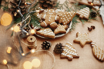 Christmas gingerbread cookies on vintage plate and anise, cinnamon, pine cones, cedar branches  with golden lights on rustic table. Baked traditional gingerbread man, tree, star cookies