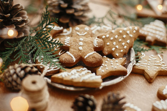 Christmas gingerbread cookies on vintage plate and anise, cinnamon, pine cones, cedar branches  with golden lights on rustic table. Baked traditional gingerbread man, tree, star cookies - Powered by Adobe
