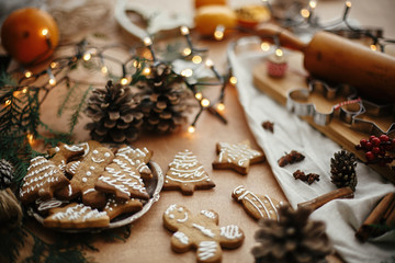 Fototapeta na wymiar Christmas gingerbread cookies on vintage plate and anise, cinnamon, pine cones, cedar branches with golden lights on rustic table. Baked traditional gingerbread cookies. Seasons greetings
