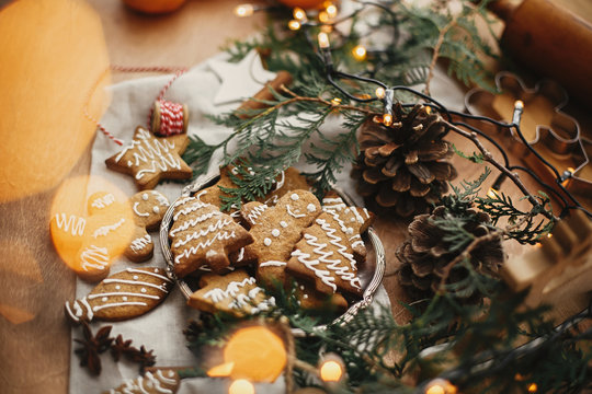 Merry Christmas. Festive gingerbread cookies with anise, cinnamon, pine cones, cedar branches and golden lights bokeh on rustic table. Atmospheric image. Seasons greetings