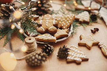 Christmas gingerbread cookies on vintage plate and anise, cinnamon, pine cones, cedar branches  with golden lights on rustic table. Baked traditional gingerbread cookies. Seasons greetings