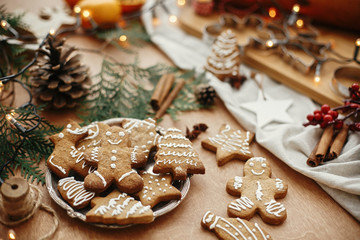 Christmas gingerbread cookies on vintage plate and anise, cinnamon, pine cones, cedar branches  with golden lights on rustic table. Baked traditional gingerbread man, tree, star cookies - Powered by Adobe