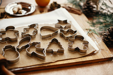 Gingerbread dough with metal cutters in different shapes for christmas cookies and wooden rolling pin, anise, ginger, cinnamon, pine cones, fir branches, flour on rustic table