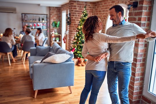 Family and friends dining at home celebrating christmas eve with traditional food and decoration, romantic couple dancing in love - Powered by Adobe