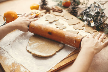 Hands rolling raw dough with wooden rolling pin on background of metal cutters, anise, ginger,...