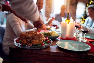 Family and friends dining at home celebrating christmas eve with traditional food and decoration, preparing turkey for dinner