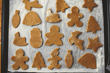 Making christmas gingerbread cookies, flat lay. Raw dough in shape of gingerbread man,christmas tree, star, deer on paper on tray, preparing for baking.