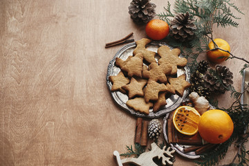 Christmas gingerbread cookies on vintage plate and anise, ginger, cinnamon, pine cones and cedar branches on rustic table with space for text. Baking traditional gingerbread cookies