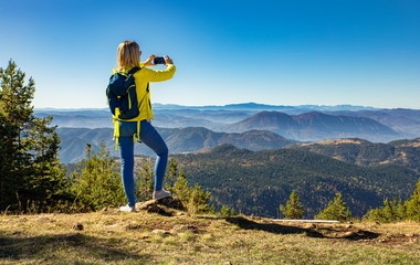 Female hiker with backpack standing on top of the mountain photographing and enjoying the view...