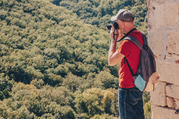 Fototapeta na wymiar Hiker in mountains taking a photo. Young man with backpack and digital photo camera.