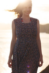 Sunny portrait of happy  young european woman. Pretty girl smiling  standing on sea beach at sunset.