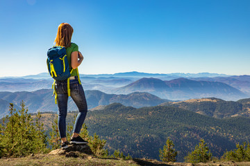 Rear view of female hiker with backpack standing on top of the mountain and enjoying the view during the day. - Powered by Adobe