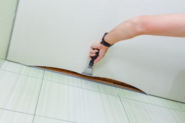Repairman installing stretch ceiling in the bathroom. Close up of man's hand with a special tool.