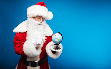 A new destination to visit. Close up photo of Santa Claus choosing with his right index finger a destination where to go on the globe, which is standing on his left hand.