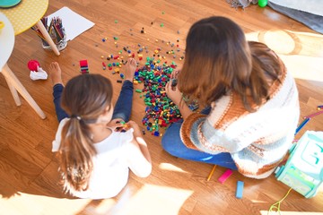 Beautiful teacher and toddler playing with building blocks toy around lots of toys at kindergarten