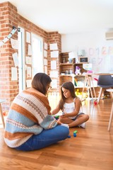 Beautiful teacher and toddler playing with wooden building blocks around lots of toys at kindergarten