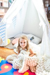 Adorable blonde toddler playing sitting on blanket inside tipi at kindergarten
