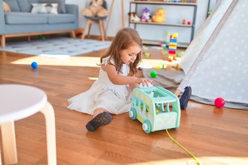 Adorable blonde toddler playing with car toy around lots of toys at kindergarten
