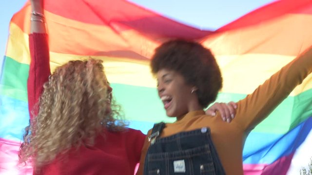 Two women friends hanging out in the city waving LGBT with pride flag