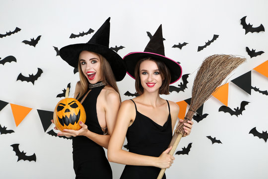 Two young women in halloween costumes with pumpkin and broom on white background
