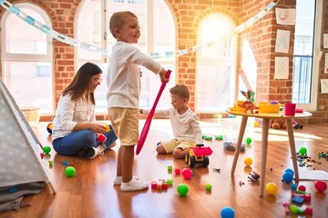 Beautiful teacher and toddlers playing around lots of toys at kindergarten