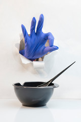 Hand in blue hairdressing gloves through a hole shows gesture all well. A black bowl with a brush is ready for staining.
