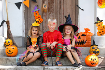 Fototapeta premium Young girls and boy in halloween costumes sitting on porch with pumpkin buckets