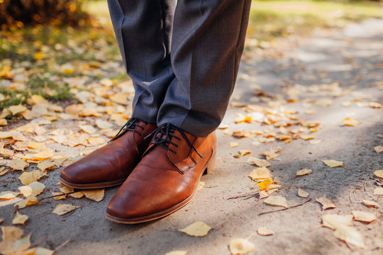 Businessman wearing shoes in autumn park. Brown leather classic footwear. Close up of legs