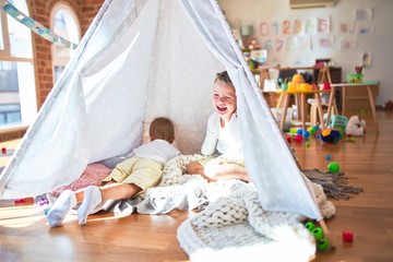 Adorable blonde twins playing inside tipi around lots of toys at kindergarten