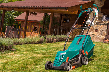 A lawn mower stands on a green lawn in the garden after work. Side view, horizontal. Concept for design, nature and landscape design. Natural background.