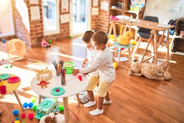 Adorable blonde twins playing around lots of toys at kindergarten