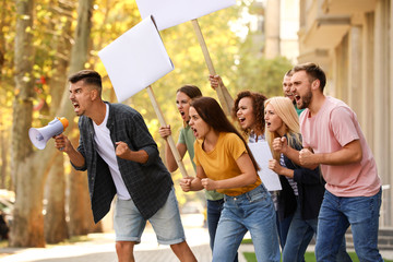 Angry young man with megaphone leading protest outdoors