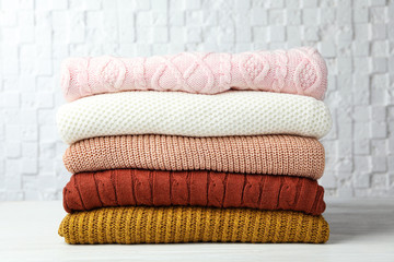 Stack of warm clothes on white wooden table against textured wall. Autumn season