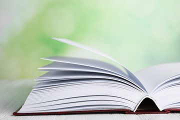 Open book on white wooden table against blurred green background, closeup