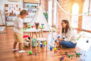 Beautiful teacher and toddler drawing using digital board around lots of toys at kindergarten