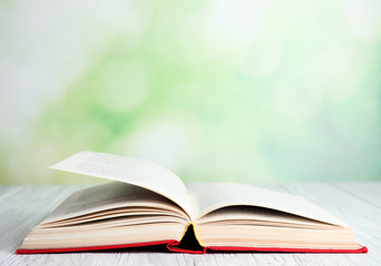 Open book on white wooden table against blurred green background. Space for text