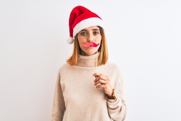 Beautiful redhead woman wearing christmas hat wearing pretend mustache over isolated background with a confident expression on smart face thinking serious