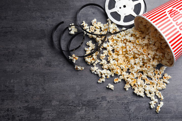 Bucket of fresh popcorn and movie reel on grey stone table, flat lay with space for text. Cinema snack