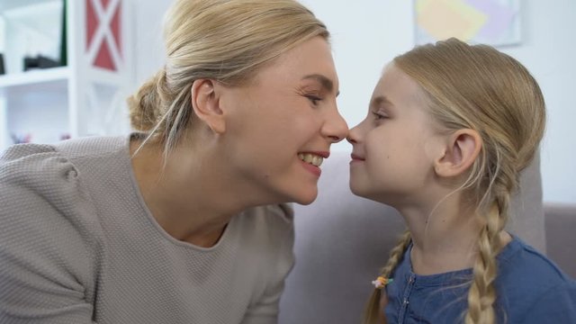 Cheerful mom playing daughters hair and touching nose, having fun together, rest