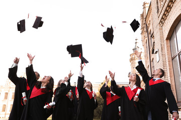Happy students with diplomas throwing graduation hats in air outdoors