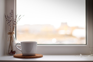 white mug of tea on the stand in front of a window on a light background