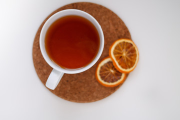autumn juicy background. on a light white background on a wooden stand is a white mug of tea, with dried oranges and red flowers.
