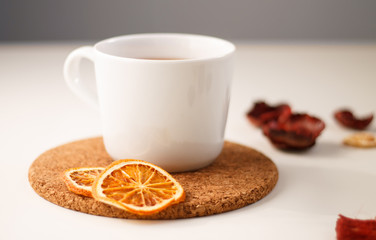 autumn juicy background. on a light white background on a wooden stand is a white mug of tea, with dried oranges and red flowers.