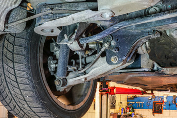 car wheel and suspension detail of lifted automobile at repair service station