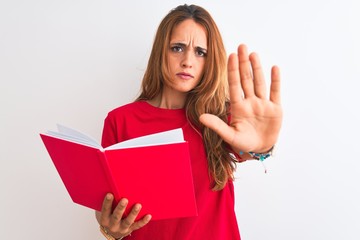 Young beautiful redhead woman reading a red book over isolated background with open hand doing stop sign with serious and confident expression, defense gesture