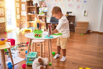 Beautiful blonde toddler drawing using digital board. Standing around lots of toys at kindergarten