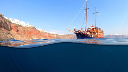 Underwater and sea level photo of tourist boat near famous bay of Ammoudi below village of Oia,...