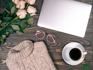 knitted sweater lies with cup of coffee, roses, laptop and glasses on wooden background